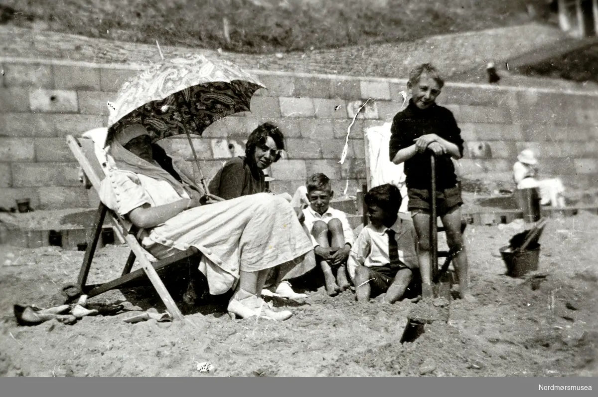 Foto fra ei badestrand, hvor vi ser en familie på fem som nyter sommeren.
Bildet er trolig fra det store utland, ukjent hvor. Datering er sannsynligvis omkring 1930 til 1939. Bildet er hentet fra fotoalbumet til Heide og kommer i serien med reg. nr. KMb-2008-022. Fra Nordmøre museums fotosamlinger.
