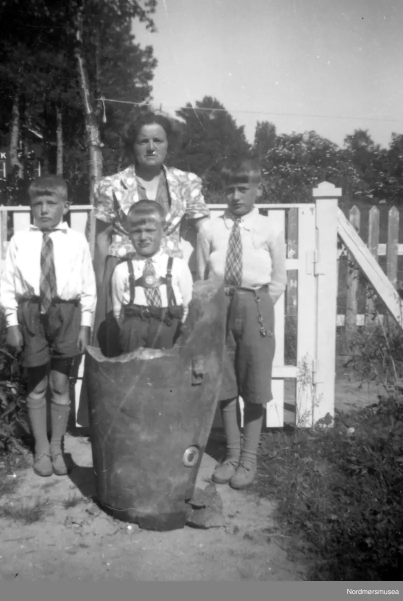 Foto fra Familien Rød, her representert med Gudrun Margrethe Rød sammen med sønnene Gunnar, Ivar og Per Olav Rød samt en halvdel av en bombe fra 1940. Bildet er fotografert i Byskogen, hvor denne halvparten av bomben falt ned. Den andre halvparten falt ned i Renabakken hvor 15 år gamle Ingolf Vatten ble drept. Det er et minnesmerke i Renabakken over denne hendelsen. Ukjent datering. Fra Nordmøre Museums fotosamlinger. Reg: EFR
