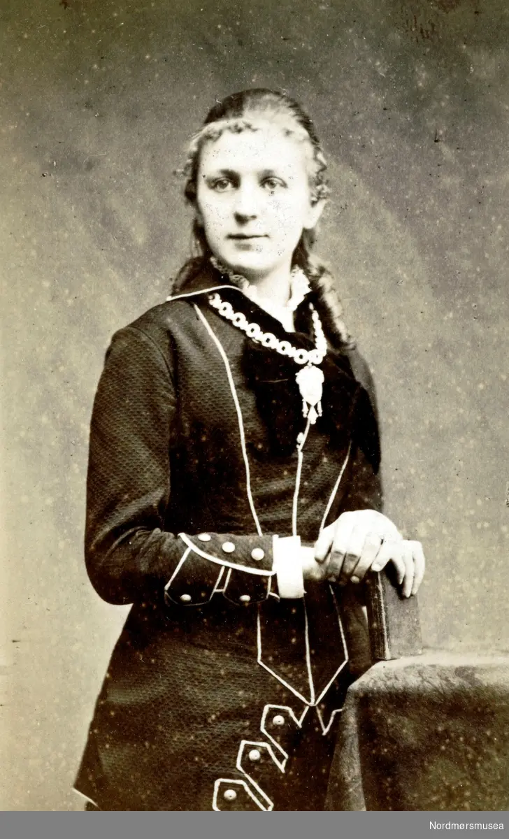 Foto trolig av Karen Kristine Johnsen (f. 1859 - d. 1937) eventuelt Anna Marie Johnsen (Mia) (f. 1862 - d. 1887). Datter av Christian Johnsen (f. 1828 - 1893) og Jensine Wilhelmine Johnsen f. Øwre (f. 1828 d. 1908). Kan også være en av de andre døtrene, men det er sannsynligvis Karen Kristine Johnsen vi ser avbildet. Fra Nordmøre museums fotosamlinger.
