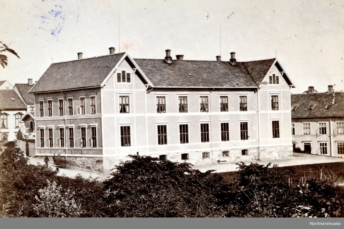 Latinskolen på Kirkelandet i Kristiansund sett fra sydvest. Til høyre skimter en litt av "Pigeskolen". Til venstre skimter en litt av Latinskolens do og Volckmars gård i Skolegata. Fra Nordmøre Museums fotosamlinger.