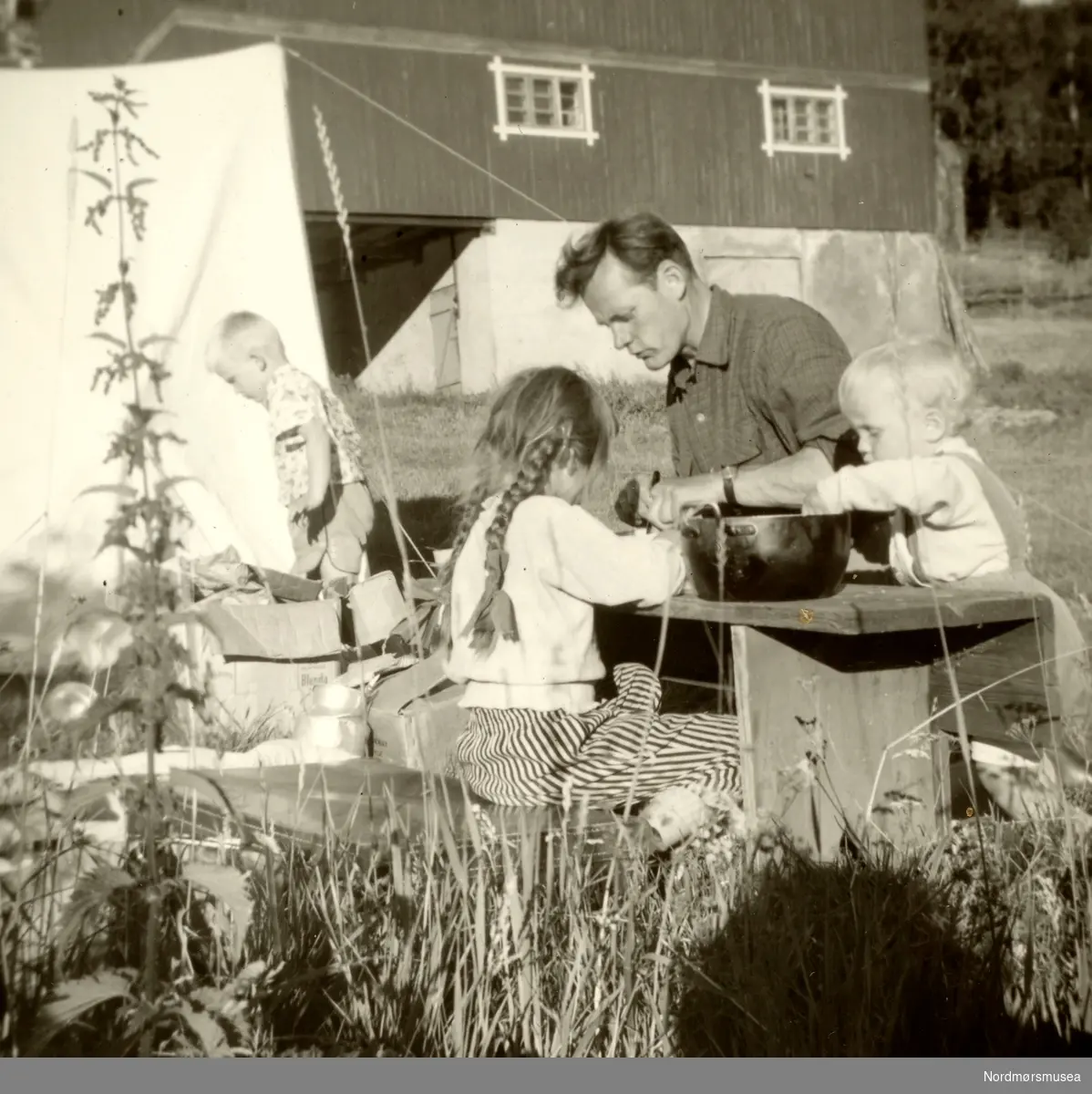 Foto av familien Knudtzon på tur. Her ser vi
Svein Waagbø Knudtzon
stående ved teltet. Deretter
ser vi Ida Margrethe Knudtzon med flettene, faren haakon Waagbø og lillebroren Terje Knudtzon
Waagbø. Trolig fra tiden rundt 1959. Ukjent hvor. Fra Ida M. Knudtzons fotosamlinger, nå en del av Nordmøre Museums fotosamlinger.
