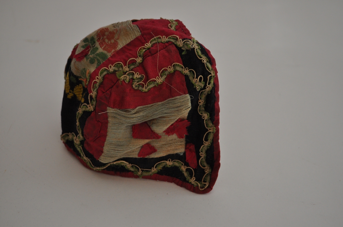 Lua er ei trebladlue med to speilvendte sidestykker og et tilnærmet rektangulært midtstykke. Hovedstoffene er av silke, sydd sammen av 15 biter. Tre biter er av lys, blågrøn silke, hvorav en bit har brosjert blomster- og bladmotiv. Fem biter er svarte, hvorav en bit har brosjert mønster i gult og grønt. Sju biter er av cerisse-rød silke, hvorav minst to er av damask. Langs kantene, sømmene og øverst på sidestykkene er lua dekorert med en blonde av hvit og grønn silketråd. På hvert sidestykke er fem små cerisse-røde silkebiter sydd fast. Ytterligere en er sydd på midtstykket bak, og det er rester etter minst en til samme sted. I skjøten mellom tre stoffbiter på midtstykket bak er det sydd på en trådrosett av lyserød og grønn silketråd, av samme materiale og type som på henglene registrert som OT.5342 AB. Lua er fôret med ubleiket linlerret, stykkene er sydd sammen og sårkantene kastet over til hver side, synlig på vranga. Framkant og nederkant er dekket av cerisse-rød silke, sydde til med lyseblå silketråd. Det er trådspor etter knyteband i lua.