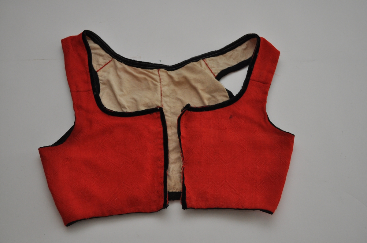 Livet er sannsynligvis et bunadliv til nasjonaldrakt. Det er sydd av et rødt, mønstervevd stoff med avanserte vevbindinger i kombinasjon. Mønsteret er dels valknuter, firkantmotiver og dels frie blomstermotiver. Livet lukkes foran med hekter og har hatt maljer. Det er kantet med svarte fløyelsband. Fôret er av ubleiket bomullslerret. Plagget består av to framstykker og to bakstykker samt seler som er sydd fast til for- og bakstykker. Framstykkene går fra midt foran til langt tilbaketrukne sidesømmer, men har et legg under hvert ermehull. Delene er sydd sammen med spilesøm med svært små sting. Kantebanda er sydd på med maskin.