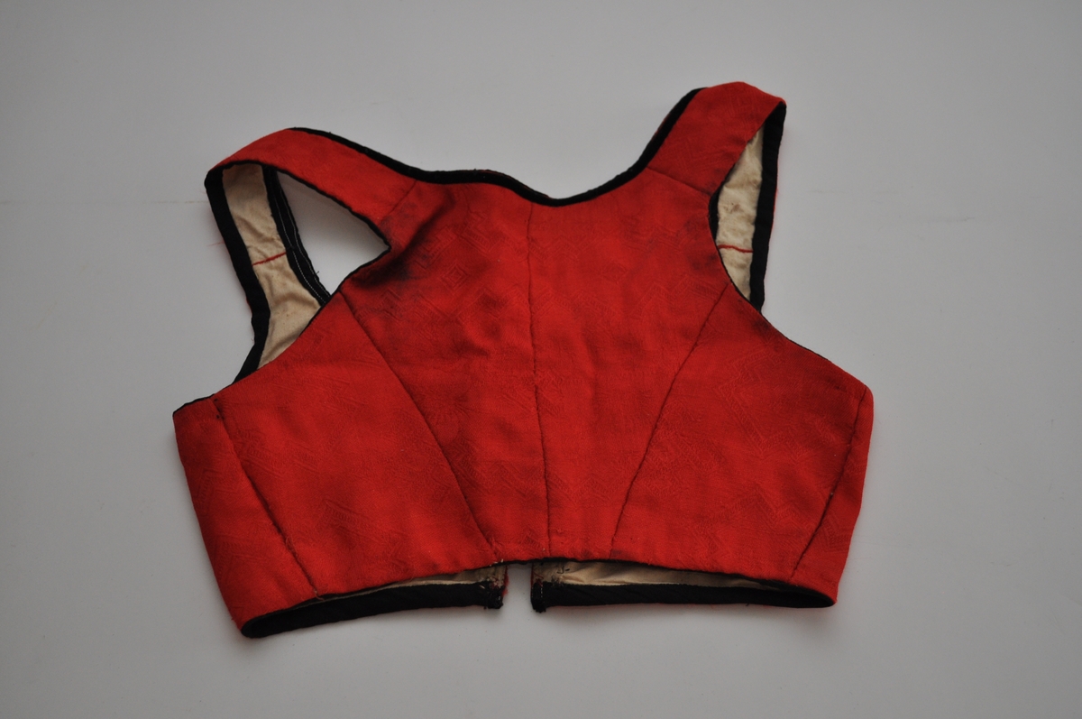 Livet er sannsynligvis et bunadliv til nasjonaldrakt. Det er sydd av et rødt, mønstervevd stoff med avanserte vevbindinger i kombinasjon. Mønsteret er dels valknuter, firkantmotiver og dels frie blomstermotiver. Livet lukkes foran med hekter og har hatt maljer. Det er kantet med svarte fløyelsband. Fôret er av ubleiket bomullslerret. Plagget består av to framstykker og to bakstykker samt seler som er sydd fast til for- og bakstykker. Framstykkene går fra midt foran til langt tilbaketrukne sidesømmer, men har et legg under hvert ermehull. Delene er sydd sammen med spilesøm med svært små sting. Kantebanda er sydd på med maskin.