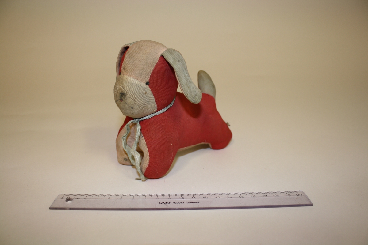 Eier: Lisbeth Andreassen Chumak
Rød og hvit tøyhund fra tidlig 1950-tall. Hunden har påtegnet snute og øyne, og et lyseblått bånd i halsen.
