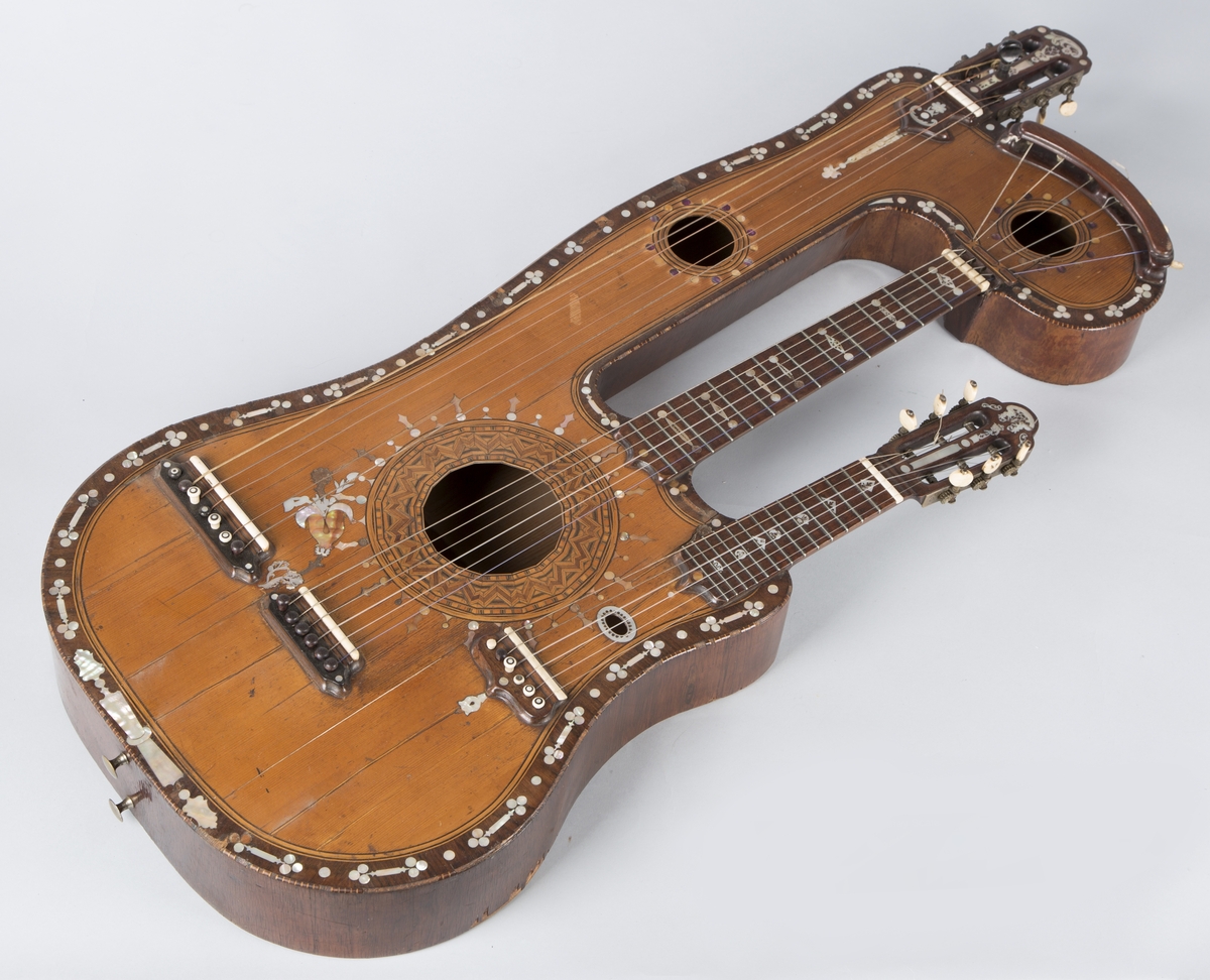 Trippelgitar, 3 halser. Lokk av gran, består av 3 deler, bunn og sarg muligens en sort mahogny. Den lengste halsen fortsetter øverst ut i en ny resonanskasse, hvis overside tjener som skruekasse for den mellomste halsen. Her er også et lydhull. En ekstra resonanseffekt oppstår ved at strengene som løper over denne resonanskassedelen under spillet svinger med. Instrumentet er utsmykket med rike perlemosrsforsiringer, delvis stekt fargede. Ornamentene er dels svært enkle og dels meget delikate blomstermønstre. Hovedlydhullet er omgitt av en 4 cm. bred krans av geometrisk intarsia, som kan minne om maurisk stil. Instrumentet har i alt 4 lydhull og 3 adskilte strengestoler. Den lengste halsen har 7 frittsvingende bass-strenger de to andre hver 6 strenger og 13 tverrbånd av metall. Runde skruehoder av elfenben. Likeså oversadler og strengestoler av elfenben.
Usignert.