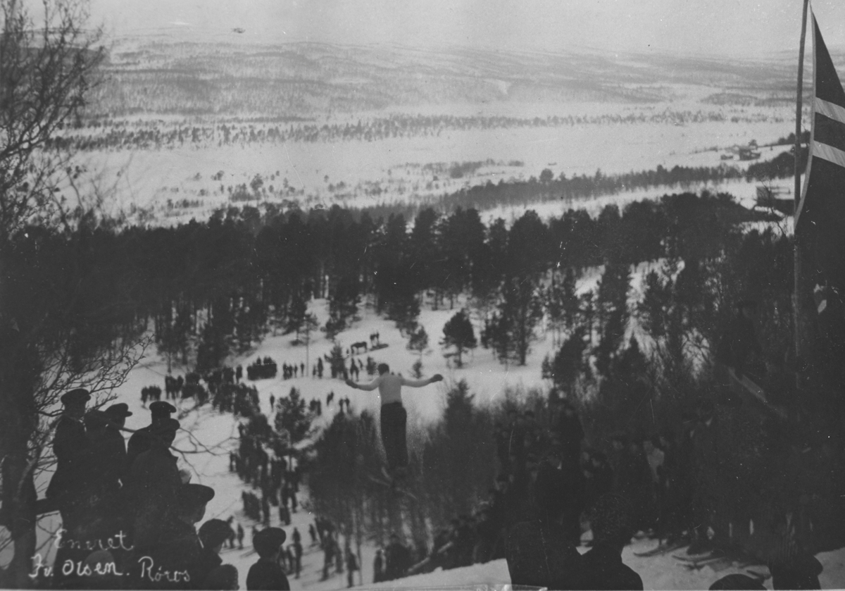 Hopper i svevet under hopprenn i Gullikstadbakken, nord for Røros. Tilskuere på begge sider av unnarennet