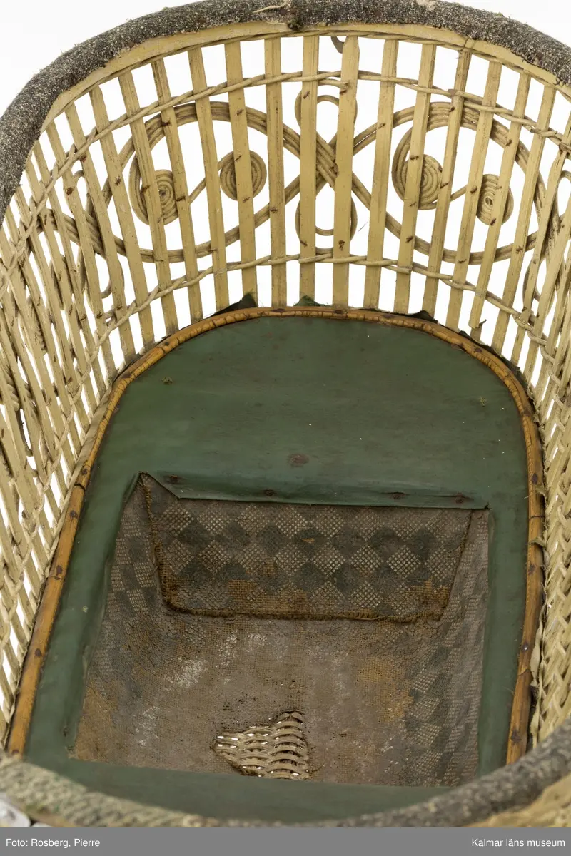 KLM 28338:1. Barnvagn, liggvagn. Hjul och underrede av metall målade i silverfärg, troligen ej ursprunglig. Två hjul är gummiklädda, ett saknar detta och det fjärde är försett med flätat naturmaterial. Handtag av vitt porslin. Vagnskorg med trästomme bestående av flätade stående och liggande spjälor målade i ljusgul nyans. Övre kanten av korgen är klädd med grovt ylletyg och på utsidan ett vävt tygband i gul ylle. Korgens botten är klädd med grönt konstläder och säckväv målat i rutmönster. I mitten av korgen en försänkning. På korgens sidor fästen för sufflett. På hjulen instansat: BRENNABOR D.R.G.M.