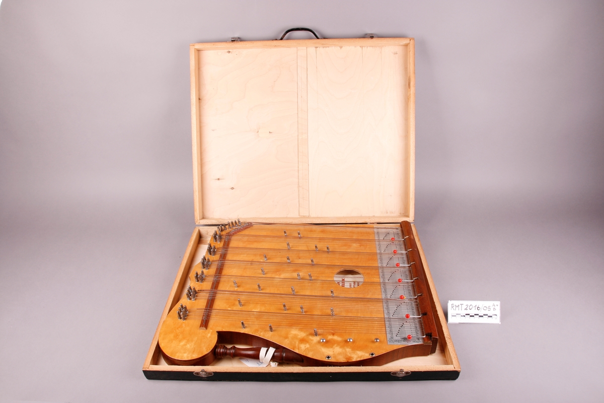 Rektangulær korpus med lokk og bunn i lysebrunt tre. Sargen er mørkt tre. Bunnen er flat. Nedre sarg er flat, og de andre tre sidene er buet. Instrmentet har en "arm" på venstre side. Fra denne armen går et håndtak i form av en søyle. Tre metallknapper på venstre side nedenfor håndtaket. Ved disse er det to metallskruer/ringer her som lager hull inn i resonanskassen. 

64 strenger som er gruppert i sju akkorder. Fra venstre: F-dur, C-dur, G-dur, D-dur, A-dur, E-dur, H-dur. Nederst på instrumentet er det påmontert et brett som beskytter strengefestet. Under strengene går det for hver akkord en stang som kan bøyes oppover. Med disse kan man forandre tersen i hver akkord, og dermed spille i moll. 

Nederst, før strengefestet og brettet er det skrudd på en metallplate som beskriver tonehøyder via notelinjer, samt notenavn. Etikett på kremhvitt (falmet?) papir er pålimt inne i kassen.