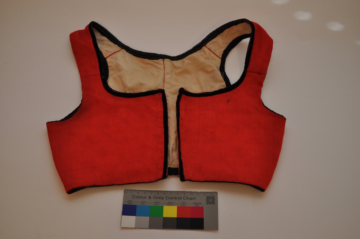 Livet er sannsynligvis et bunadliv til nasjonaldrakt. Det er sydd av et rødt, mønstervevd stoff med avanserte vevbindinger i kombinasjon. Mønsteret er dels valknuter, firkantmotiver og dels frie blomstermotiver. Livet lukkes foran med hekter og har hatt maljer. Det er kantet med svarte fløyelsband. Fôret er av ubleiket bomullslerret. Plagget består av to framstykker og to bakstykker samt seler som er sydd fast til for- og bakstykker. Framstykkene går fra midt foran til langt tilbaketrukne sidesømmer, men har et legg under hvert ermehull. Delene er sydd sammen med spilesøm med svært små sting. Kantebanda er sydd på med maskin.