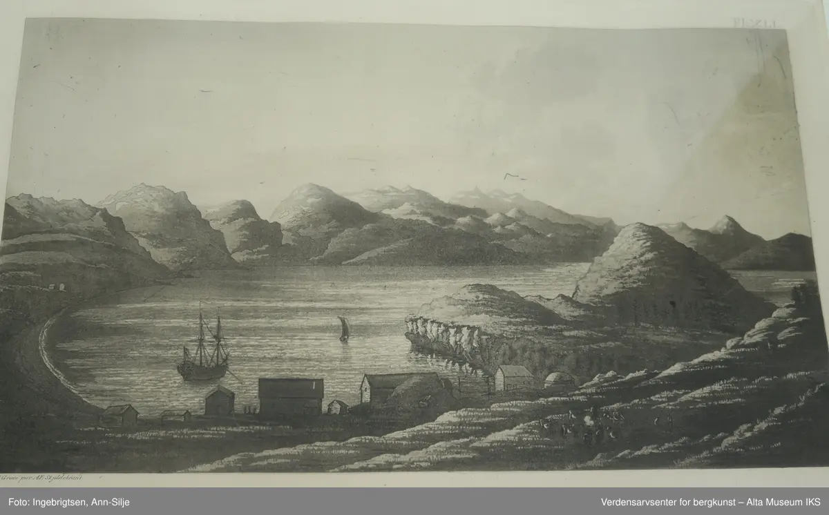 Rektangulær ramme med sort-hvitt bilde over havnen i Bossekop, Alta. I forgrunnen er Nilsen-berget og 9 bygninger i ulike størrelser. I selve havnen er det et stort seilskip og litt lenger unna er det en mindre båt med seil. I bakgrunnen er fjellene på vestsiden av Altafjorden.