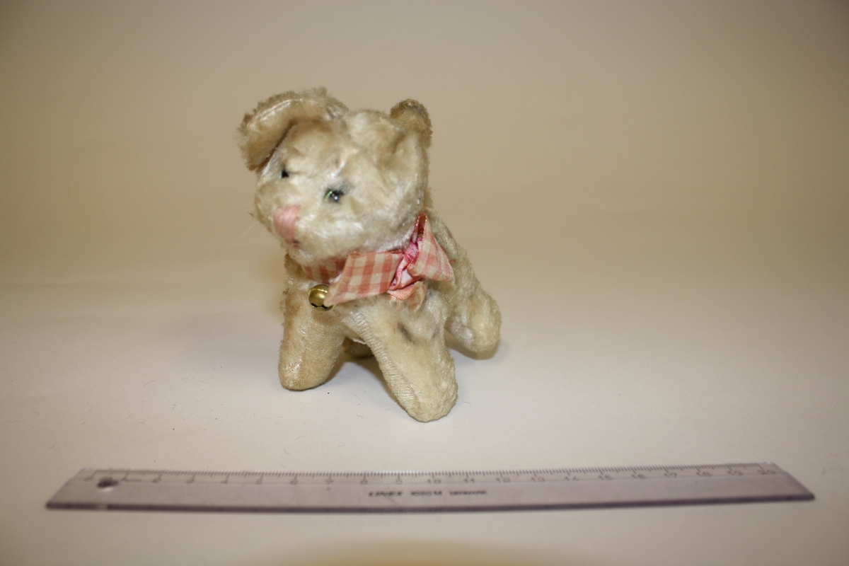 Gitt av Lisbeth Andreassen Chumak. Liten katt med rutete sløyfe med bjelle. Fra 1950-tallet. Beigebrun farge på katten. Opprinnelig hvit.