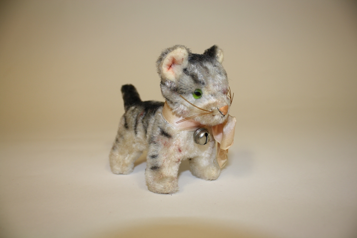 Gitt av Lisbeth Andreassen Chumak. Gråstripete katt med bjelle og rosa sløyfe. Fra 1950 tallet.