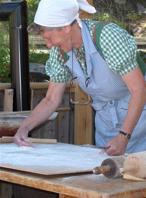 Dame står ute og baker flatbrød. Her fordeler hun mel utover bakstbordet.
