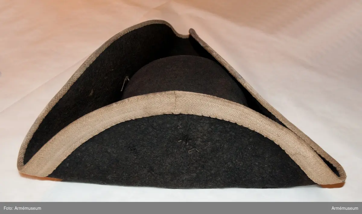 Trekantig hatt av svart filt med vitt band utmed brättet.