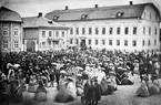 Bilden är tagen den 15 maj 1864 på det då betydligt mindre Stora Torget som var utsträckt i nord-syd med Västra (då södra) Torggatan i bildens högerkant. Till vänster ser vi en del av residenset med landskontoret till höger om portalen och mitt i bild dominerar Frimurarlogen på samma tomt som nuvarande byggnad. På bilden överlämnar fruntimmersdeputerade Euphrosyne Nygren ett standar till kapten Sparre i skarpskyttekåren.