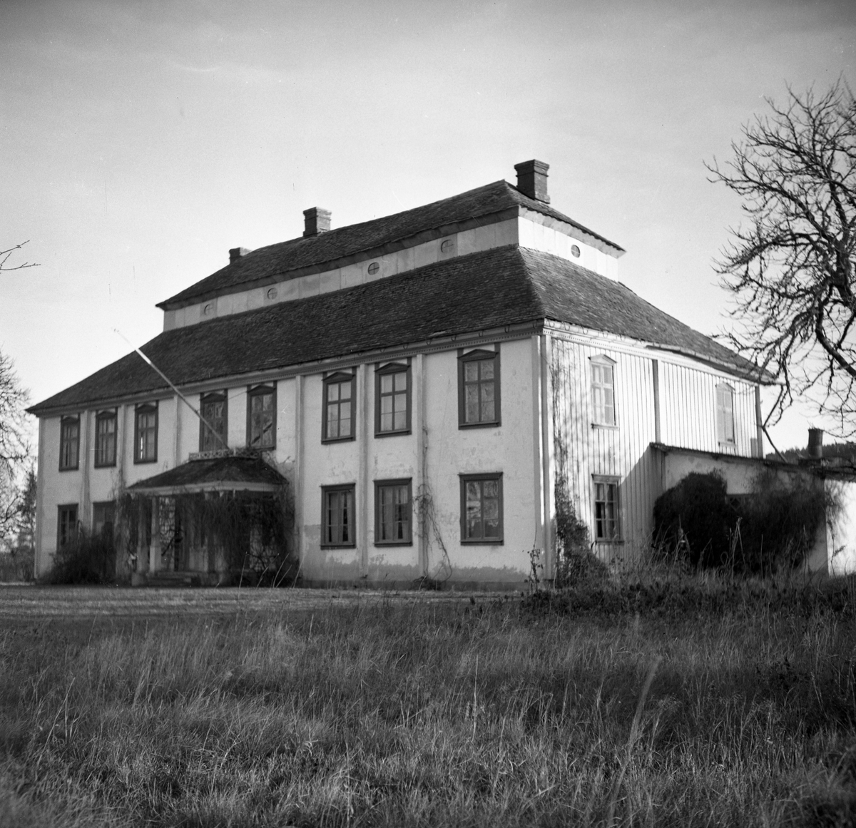 Karolinsk herrgårdsbyggnad, locklistpanelat och rödfärgat timmer i två våningar, säteritak med mösterlagt skiffer från Glava.
