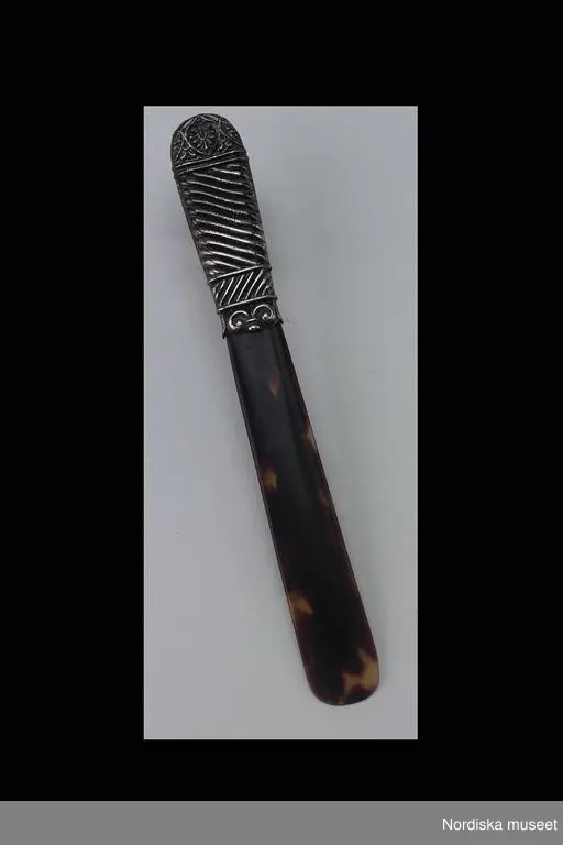Huvudliggaren:
"Brevkniv, sköldpadd, metall. Runt blad, skaft mönsterpressad silver. Från markis Lagergrens skrivbord. Tillverkad före 1930."
