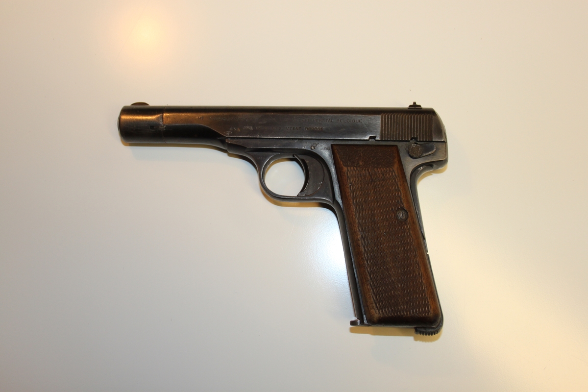 Brunt deksel på hver side av pistolskaftet. Med «Rutemønster». Festet med gjennomgående skrue. Magasin sitter i.