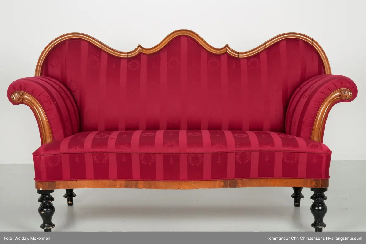 Akantusdekor i treverket. Dekor m/possementsnorer. Baksiden av sofaen er laget av et billigere treslag, der det ikke synes. Sofaen er nok ment å stå inntil en vegg. Grønt stoff ble brukt som underlag før det røde.