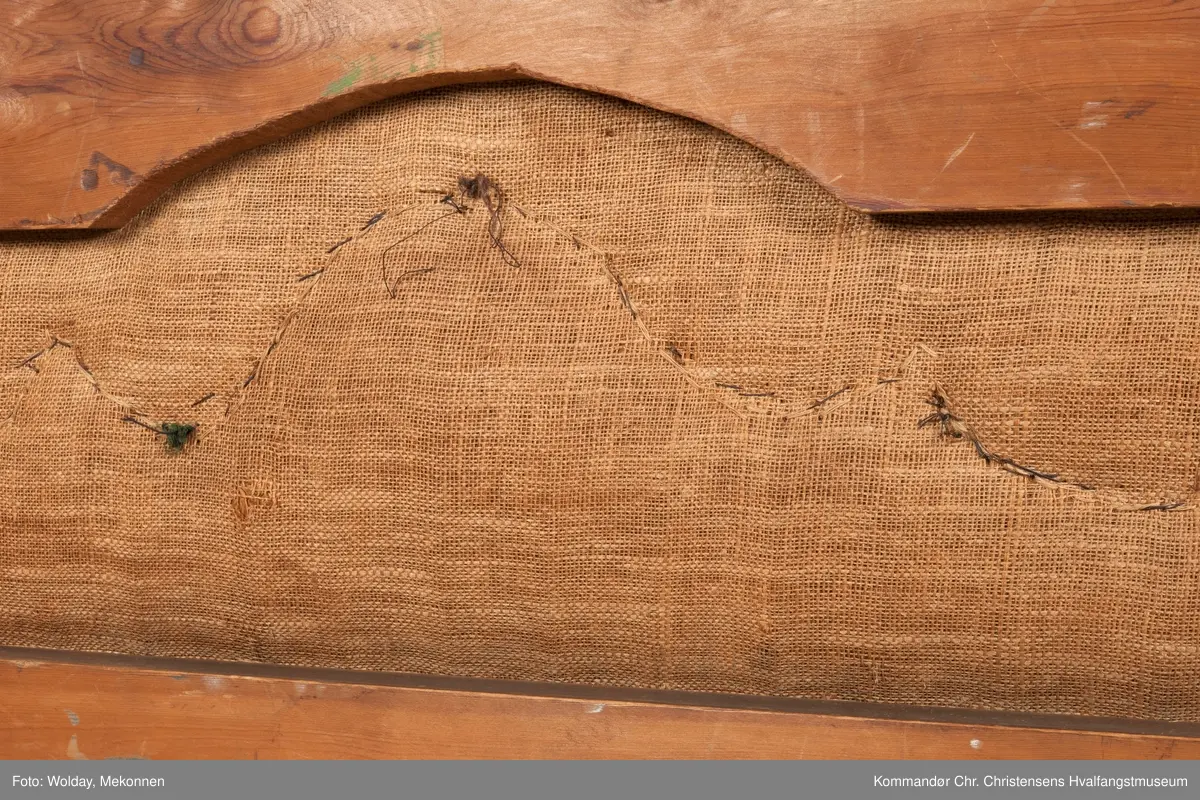 Akantusdekor i treverket. Dekor m/possementsnorer. Baksiden av sofaen er laget av et billigere treslag, der det ikke synes. Sofaen er nok ment å stå inntil en vegg. Grønt stoff ble brukt som underlag før det røde.