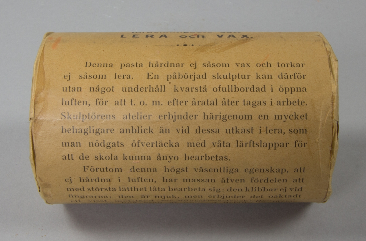 Plastelinamaterial, 6 st. 4 st cylindriska i obrutna förpackningar med brunt omslagspapper och lång reklamtext. 2 st utan omslagspapper och använda till häften. Ovanpå en av dem klumpar av plastelina.