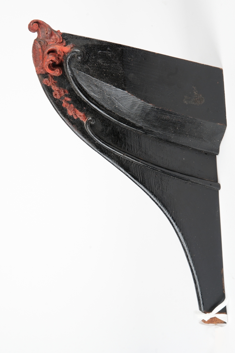 Okänt fartyg. Vapensköld med räfflad botten, krönt av volut och omgiven av blad och bladslingor. Monterad till stävkonstruktion av svartmålat trä. Bottenplattan saknas. Röd vax.