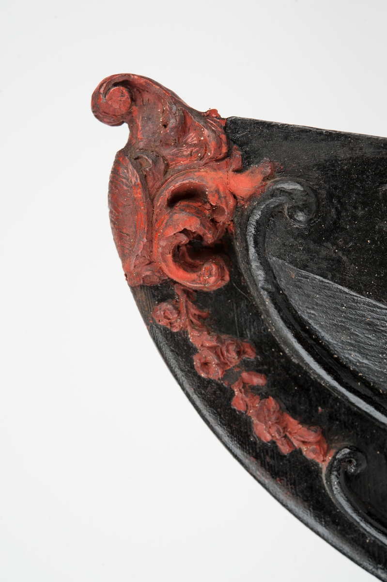 Okänt fartyg. Vapensköld med räfflad botten, krönt av volut och omgiven av blad och bladslingor. Monterad till stävkonstruktion av svartmålat trä. Bottenplattan saknas. Röd vax.