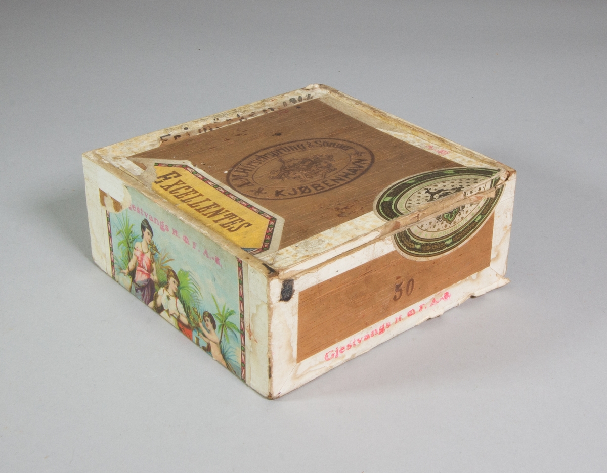 Sydonsask, fd cigarrlåda, av trä kvadratisk med fällock. Innehåller bland annat en rulle med gul tråd, en del av en tändsticksask omlindad med svart tråd, en del av en tändsticksask omlindad med beige tråd och två synålar samt trasig lornjett med guldfärgade bågar. På lockets insida påklistrat frimärke 10 öre med Gustav V:s bild, rött.