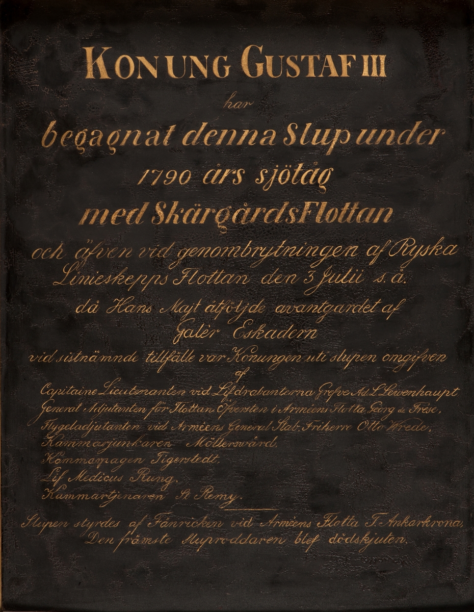 Minnestavla i koppar, svartmålad med inskription i guldskrift. Ram av förgyllt trä. Överstycke med 2 delfiner förande neptunigaffel.