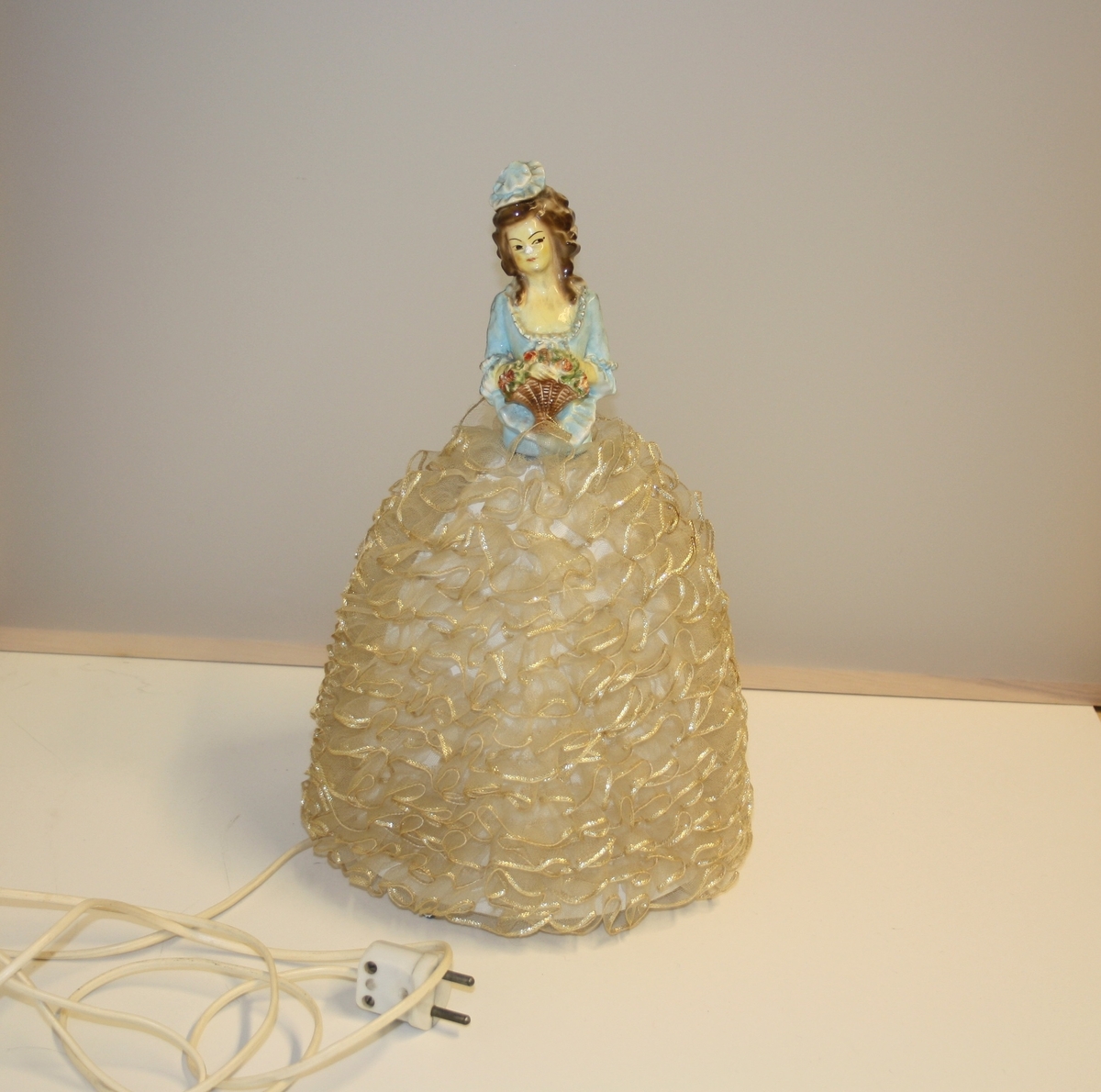 Lampe med skjerm med gipsfigur på toppen. 
Blonder utanpå skjermen (som blir kjolen til dokka)