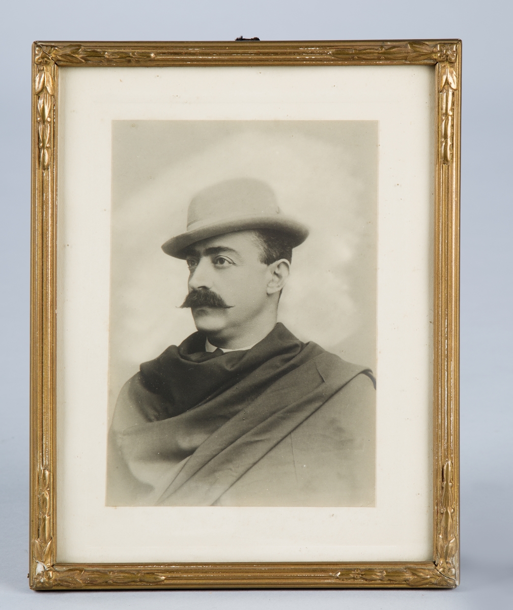 Svart-hvitt fotografi satt i glass og ramme. Rammen har relieffmønster og er forgylt.