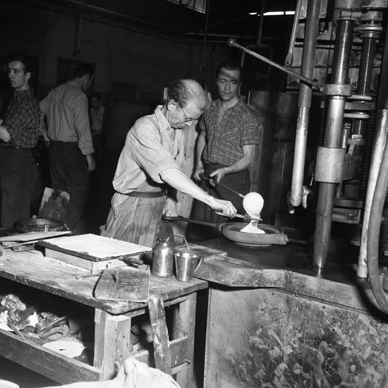 Lindshammars glasbruk. 1956. Rätt mängd glas klipps av inför momentet pressning.