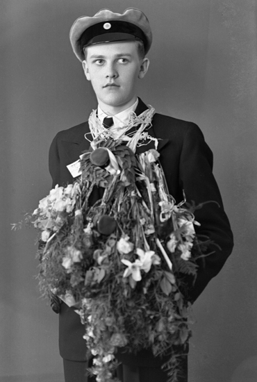 Foto av en ung i mörk kostym, som just tagit realexamen.
Knäbild. Ateljéfoto.
Trol. Viktor Hugo Ingvar Iselau (1922-2002), Alvesta.
Källa: Sveriges Dödbok 1901-2009.