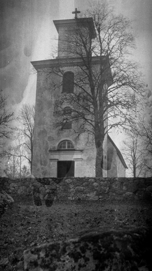 Foto på en kyrka framifrån med en stenmur utanför.