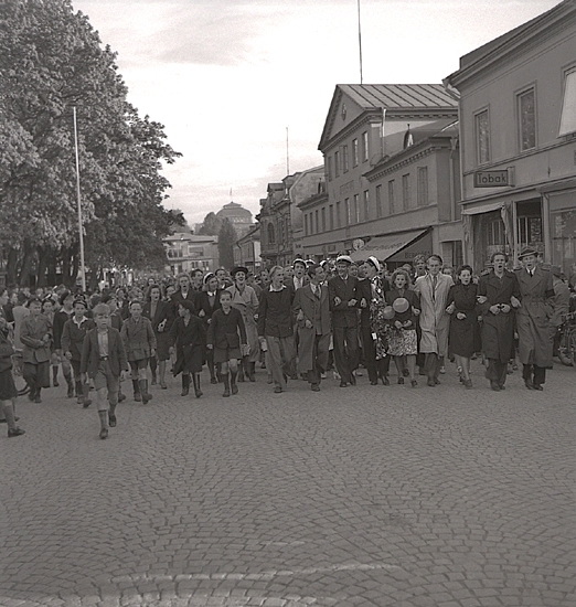 Studenterna 1940. 31/5 - 1/6. 
Studenter och anhöriga m.fl. på Kungsgatan, på väg norrut. I bakgrunden skymtar dåv. järnvägsstationen och kupolen till dåv. Växjö Högre Allmänna Läroverk.