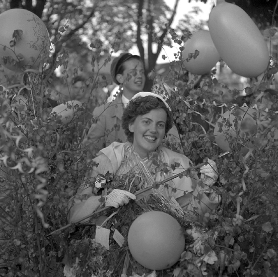Studenterna första dagen, 1950.
En glad kvinnlig student, omgiven av lövruskor och ballonger.
Bakom henne syns en ung man i s.k. realmössa.

Angående avgångsklasserna 1950 - se "Lärare och Studenter vid Växjö 
Högre Allmänna Läroverk 1850-1950" (1951), s. 193-196, 289.