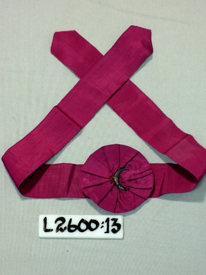 Ett 40 mm brett vinrött/cerise ripsband med en bandros på mitten 
(diam.80 mm)
Mitt i rosen en krönt halvmåne av vit metall.
Trol. Frimurarorden. 
Inskrivet i huvudboken 1933
Funktion: Ordenstecken