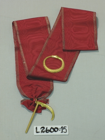 Ett 100 mm brett ripsband med silverkanter. På bandet en förgylld orm,
(metall) som biter sig i stjärten. Vidhängd förgylld lie (metall).
Frimurarorden (?). 
Inskrivet i huvudboken 1933
Funktion: Ordenstecken