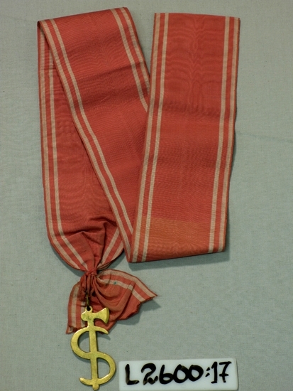 Ett 70 mm brett ripsband (vit-rosa-vit-rosa-vit-rosa-vit). Vidhängande 
bila med ett "S" omkring (metall).

Inskrivet i huvudboken 1933
Funktion: Ordenstecken