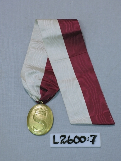 Ett 70 mm brett ripsband, rött och vitt, med en gul metallmedaljong. 
Mönster;  ett krönt S.

Inskriven i huvudboken 1933.
Funktion: Ordenstecken