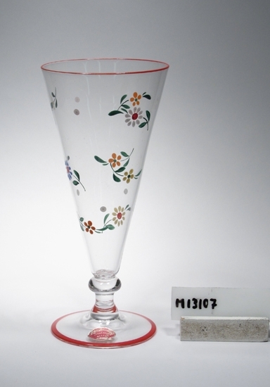Blomglas med rund fot.
Beskrivning: Målat i rött, grönt, gult, blått , vitt och brandgult, 
kring foten och vasens överkant röd rand. Hela vasen översållad 
med små blommor och blad.
Färg: Ofärgat klarglas.
Mått: Ovan angivna diameter avser övre diameter. Fotdiameter: 73 mm.
Inskriven i huvukatalogen 1943.
Funktion: Blomvas