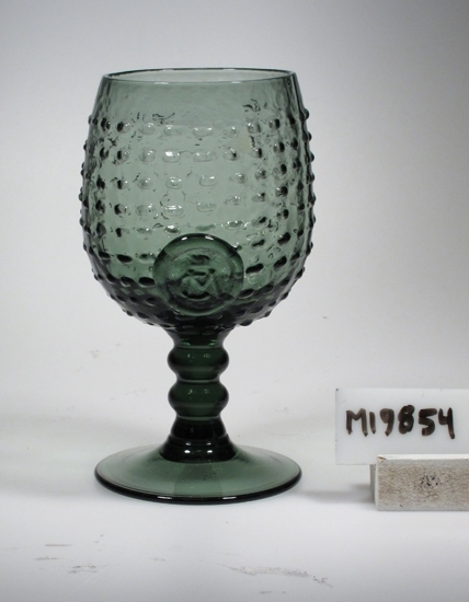 Vinglas. Rekonstruktion (souvenir) av glas från Hertig Carls hytta, Nyköping 1580-talet. Troligen tillverkat på Reijmyre glasbruk.
Beskrivning: Sluten, äggformad kupa. Kort ben med två vulster. Insvängd, konisk fot. Hela kupan täckt med regelbundet placerade prickar i relief. Påklippt, runt sigill med krona och monogram C.M. (bokstäverna ovanpå varandra). (Se även Signering, märkning" ovan. Färg: Grågrönt, relativt klart, sodaglas. Teknik: Kupan blåst i form. Påklippt sigill. Mått: Ovan angivna diameter avser glasets övre diameter. Fotdiameter: 65 mm Inskrivet i huvudkatalogen ? Funktion: Vinglas