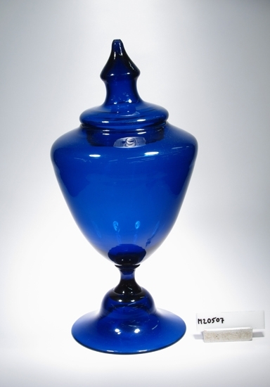 Urna med lock.
Färg: Koboltblått klarglas.
Mått: Ovan anges höjd med lock samt fot/bottendiameter.
Inskrivet i huvudkatalogen 1968.
Funktion: Prydnadsurna