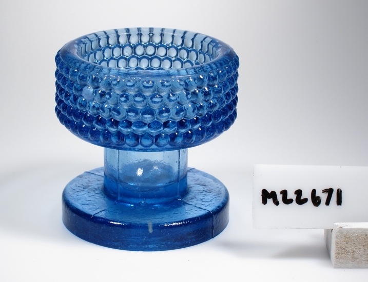 Ljusstake.
Tillverkad på Sölvesborg, Sölvehyttan.
Beskrivning: Cylinderformad kupa. Ihåligt, rakt "ben". Skivfot. Kupan täckt med tätbelagda kulor.
Färg: Koboltblått, tämligen klart glas.
Mått: Ovan angivna diameter avser ljusstakens övre och nedre diameter.
Inskrivet i huvudkatalogen 1974.
Funktion: Ljusstake