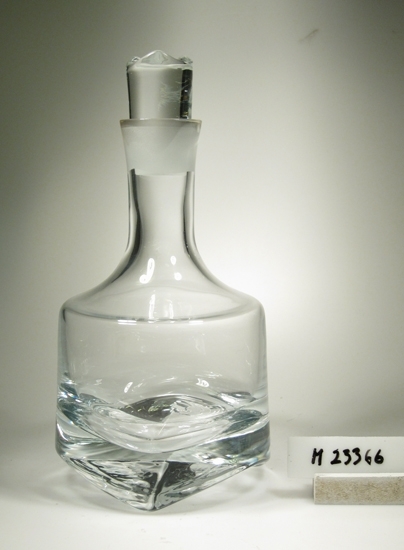 Karaff med propp. Tillverkat av Krona Bruken. Åseda glasbruk.
Formgivare: Bo Borgström.
Beskrivning: Något konad hals, starkt markerad skuldra, konad kropp (nedåt förlagd vidd).  
Tjock botten med tre uddar. Närmast cylindrisk propp med tre uddar.
Färg: Ofärgat klarglas. Kristallglas?
Mått: Ovan angivna höjd är med propp, utan propp: 206 mm.
Proppens diameter: 34 mm.
Bottnens största diameter: 125 mm.
Fyrkantig, svart etikett med en krona och text i guld: Se "Signering, märkning" 1 ovan.
Avlång guldetikett med text: Se "Signering, märkning" 2 ovan.
Inskrivet i huvudkatalogen 1975.

Ur "Glas 75" utställningsglas.
Funktion: Karaff