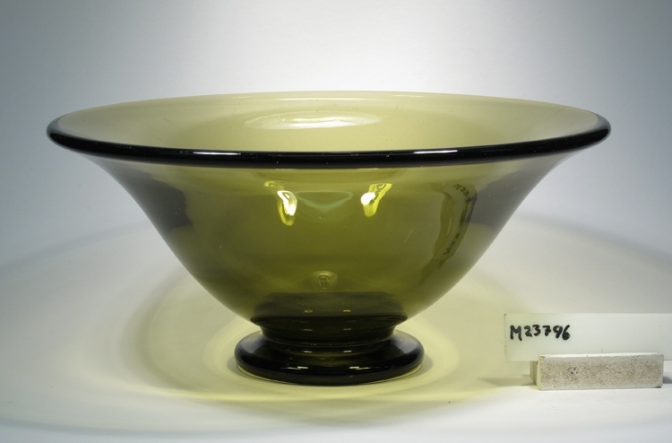 Skål på fot.
Beskrivning: Klockformad skål på fot med avrundad kant. Stor kula i botten.
Färg: Olivgrönt klarglas. Några små blåsor i massan.
Mått: Ovan anges övre diameter. Fotdiameter: 95 mm.
Inskrivet i huvudkatalogen tidigast 1978.
Funktion: Skål