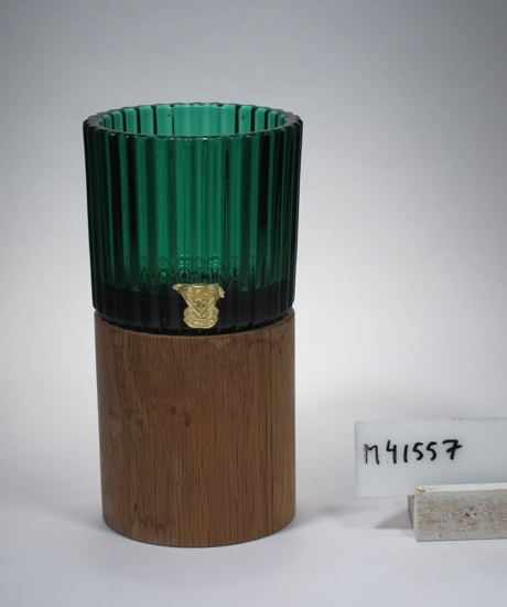 Ljuslykta på träfot. Art.nr. KB 62/24, 1962. 
Beskrivning: Cylindrisk, pressad kupa, svagt konisk fot. Ett blomformat hål i botten.Träfoten är cylindrisk med hål överst för plats för ljuslyktan. Dekor: Räfflad utsida på kupan.
Färg: Grön ljuslykta, klarglas. Träfärgad fot.
Mått: Ovan anges ljuslyktans höjd och övre diameter. Fotdiameter: 48 mm. Träfotens höjd: 65 mm. Övre och nedre diameter: 60 respektive 60 mm.
Firmamärke på ljuslyktan; gult med text. Se "Signering, märkning" 1 ovan. Lapp på foten; vit med blå ram.Se "Signering, märkning" 2 ovan.
Inskrivet i huvudkatalogen 1980.

Kataloger:
Finns i 1963 års katalog sid 23, 1970 års katalog sid 19, utan fot.

Arthur Percy (1886-1976), konstnär, designer. Verksam på Gullaskruf från 1952. 
Kjell Blomberg (1931-), designer m.m.. Verksam vid Gullaskruf 1954-1977.
Funktion: Ljuslykta