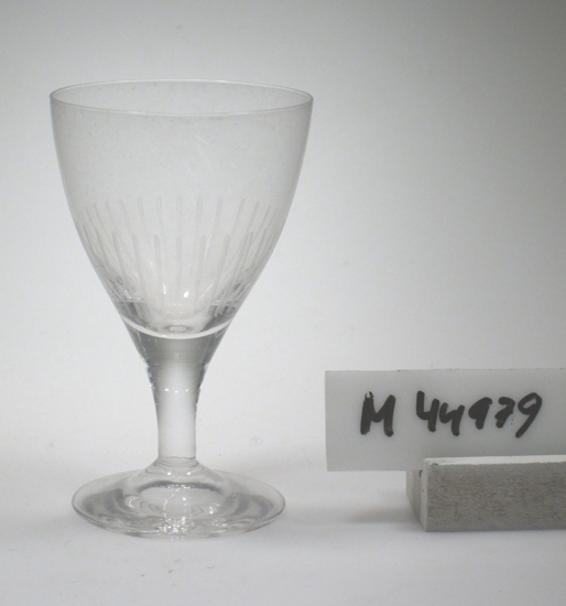 Starkvinsglas i ofärgat glas.
Kupan är konisk och svagt böjd.
Relativt kort ben. 
Sllipade stående linjer på kupans nedre del.
Finns med i katalogerna 1956 och 1962.
Funktion: Starkvinsglas