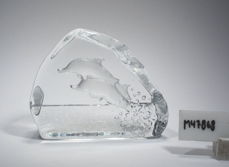 Glasblock med delfiner.
Formgivet av Rune Strand? Möjligen tillverkat under 1990-talet.
Beskrivning: Flat glasskiva med oregelbunden kant. Motiv i form av hoppande delfiner.
Färg: Ofärgat klarglas.
Teknik: Stöpt och blästrat.
Inskrivet i huvudkatalogen tidigast 1995.
Funktion: Glasblock, prydnadsföremål.
